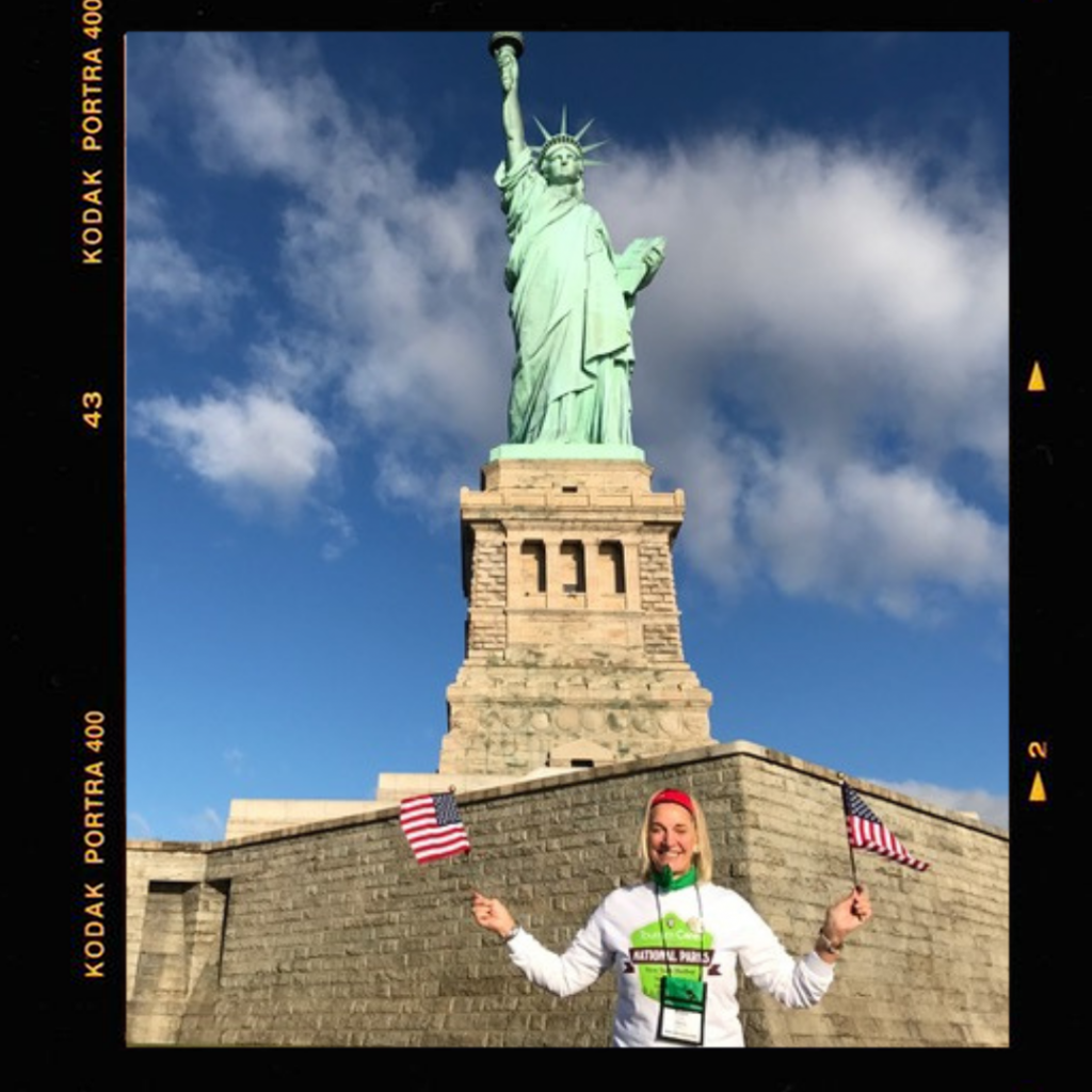 robin-tauck-waving-usflag in front of statue of liberty